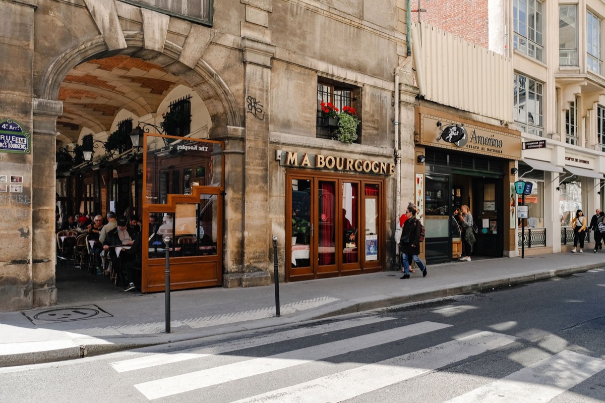 uma rua francesa com pessoas caminhando e um sinal de café