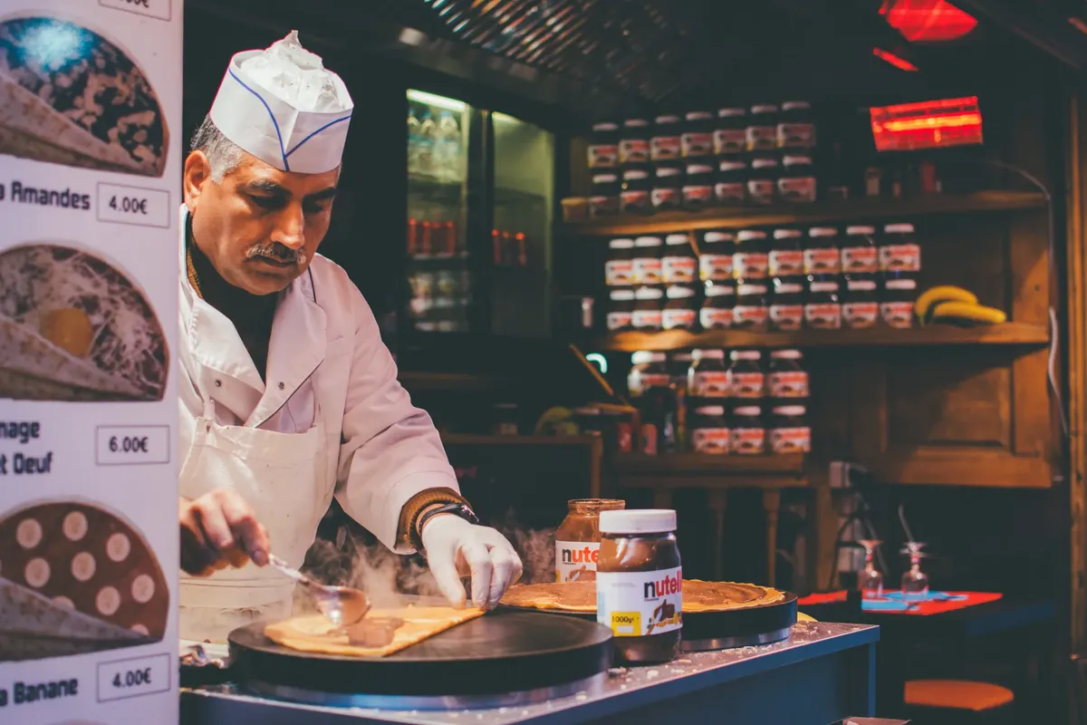 A chef skillfully prepares a Nutella crepe in a cozy Parisian café. Indoor ambiance and culinary expertise.