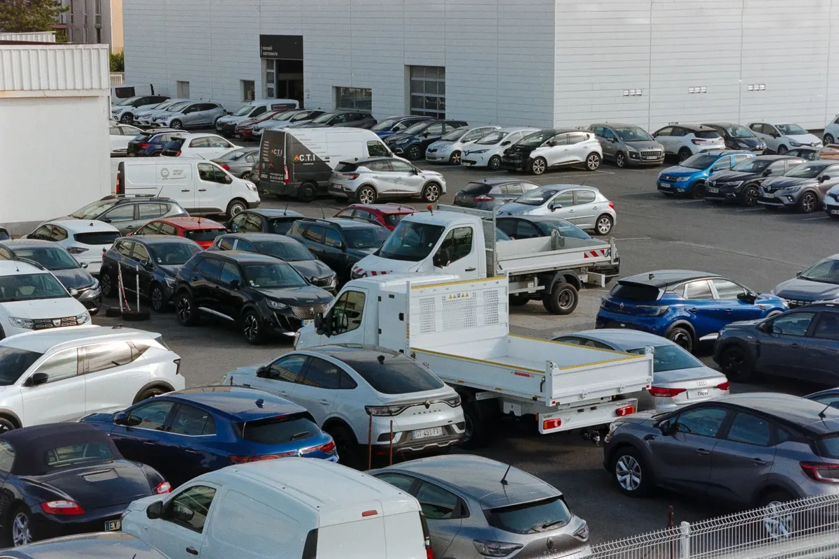 A crowded parking lot in Compiegne, France, featuring various parked cars and vans on a sunny day.